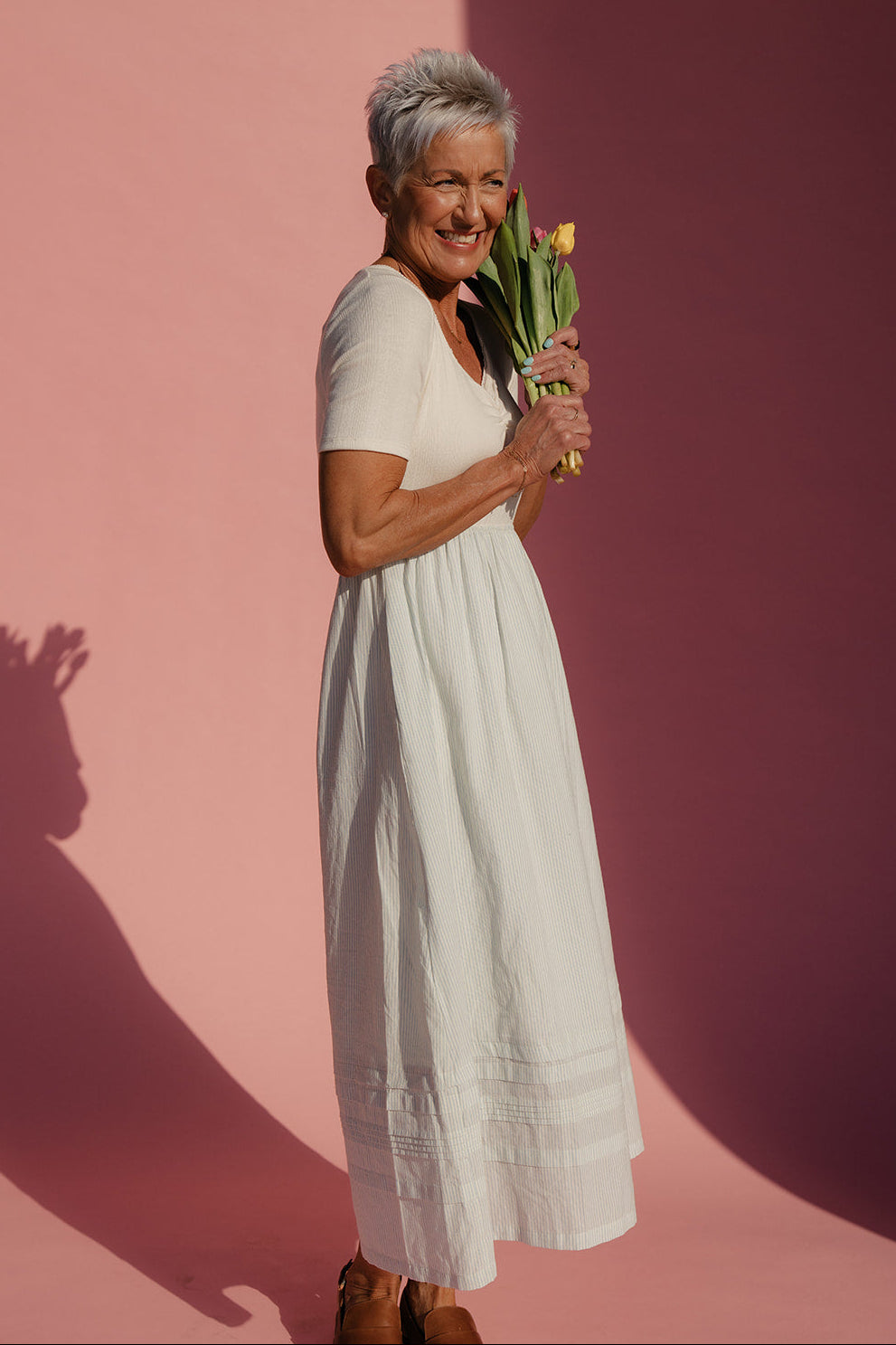 Woman in a white dress holding flowers against a pink background