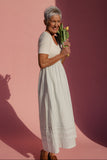Woman in a white dress holding flowers against a pink background