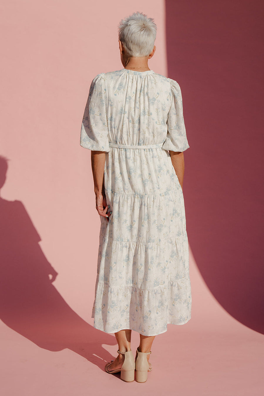 Woman wearing a white floral dress against a pink background