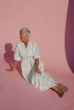 Woman in a white floral dress sitting on a pink background