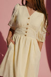 Woman wearing a light yellow dress with button details against a pink background
