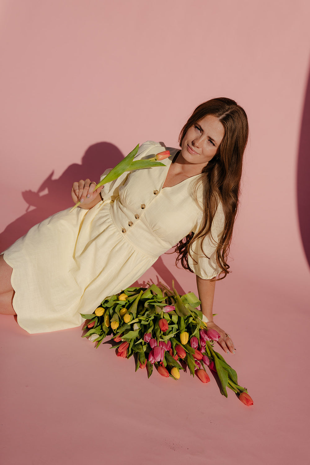 Woman in a white dress holding flowers against a pink background
