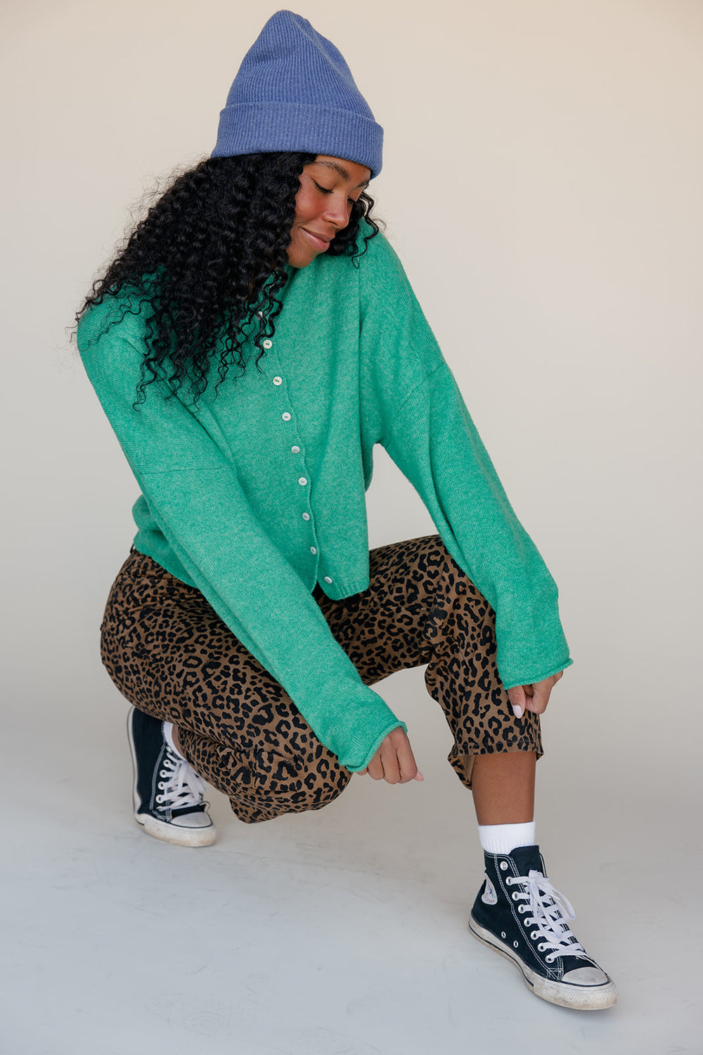 Person wearing a green sweater, leopard print pants, and a blue beanie on a plain background