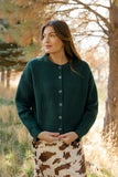 Woman wearing a green coat standing in a forested area