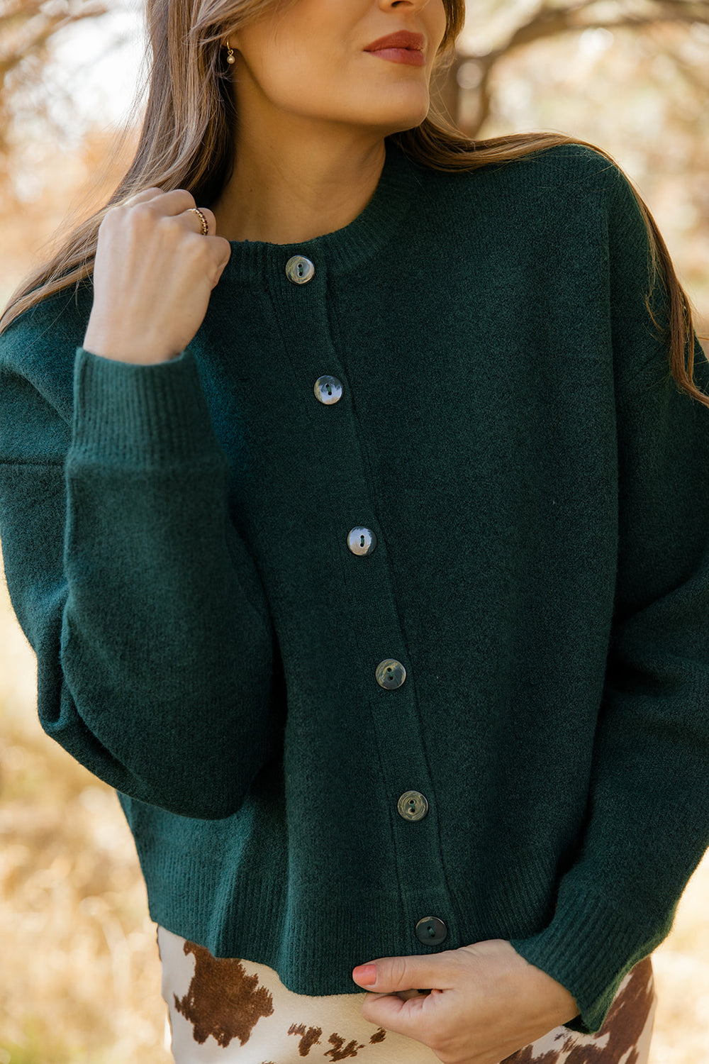 Woman wearing a dark green cardigan with a blurred natural background