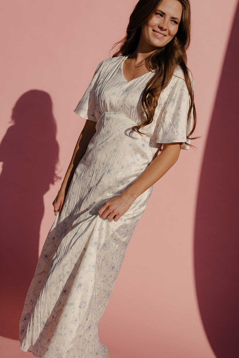 Woman in a light dress standing against a pink wall