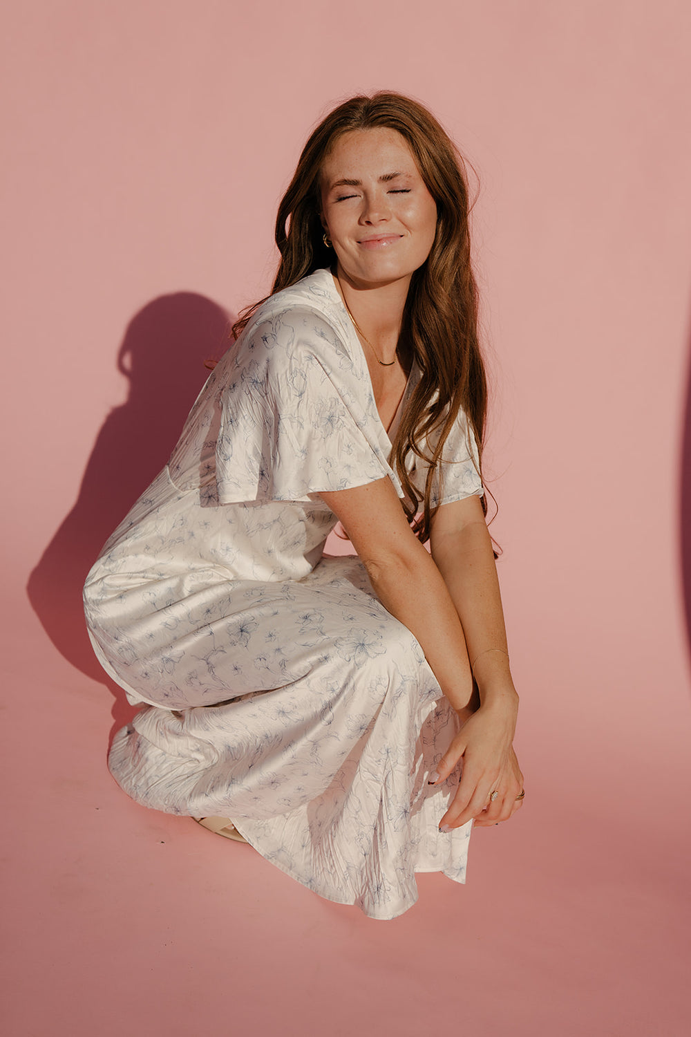 Woman in a white dress sitting on a pink background