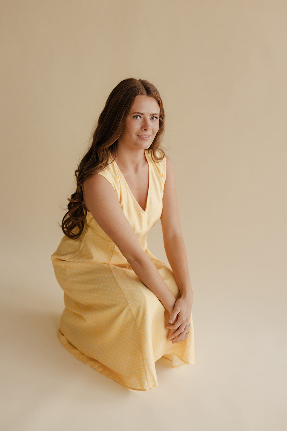 Woman in a yellow dress sitting on a beige background