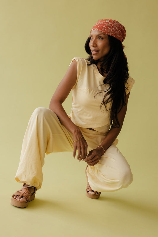 Woman in a yellow outfit with a red headscarf sitting on a yellow background