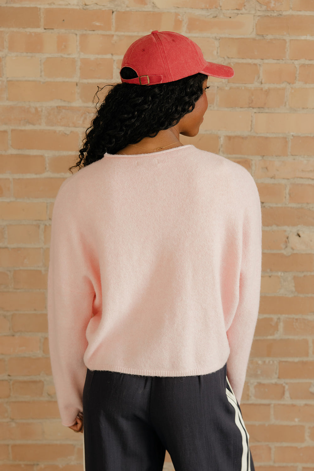 Person wearing a pink sweater and red cap against a brick wall
