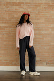 Person wearing a pink sweater and black pants standing against a brick wall.