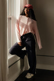 Woman in pink sweater and black pants leaning against a window