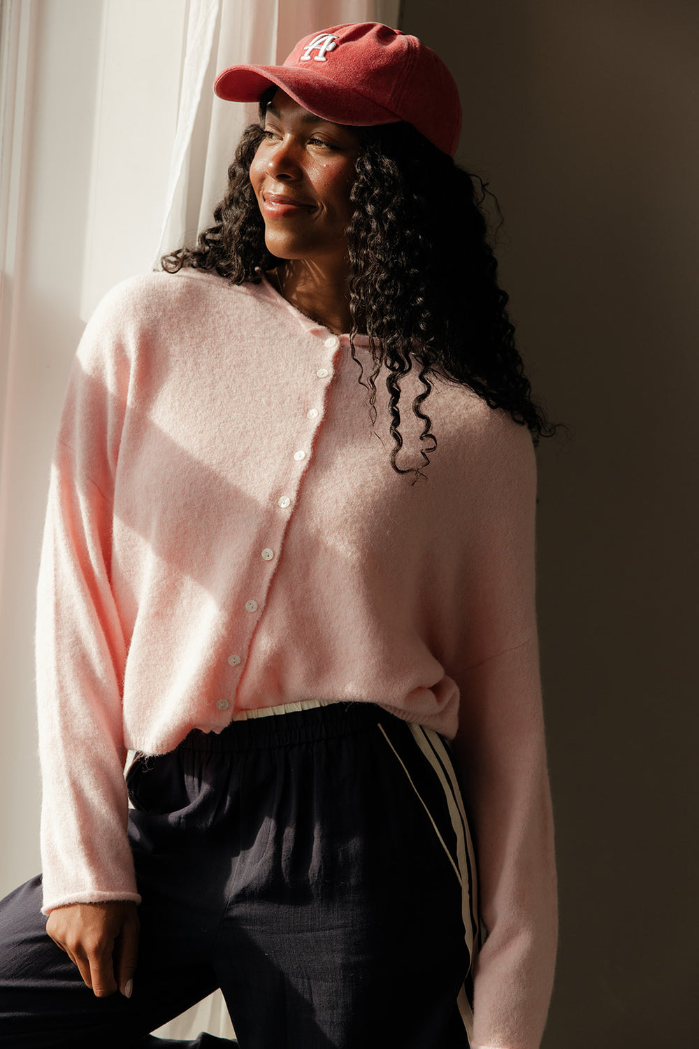 Woman wearing a pink cardigan and red cap indoors with a neutral background