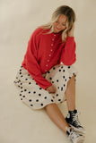 Woman wearing a red sweater and polka dot skirt with high-top sneakers on a plain background