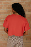 Person wearing a red t-shirt and checkered pants against a brick wall.