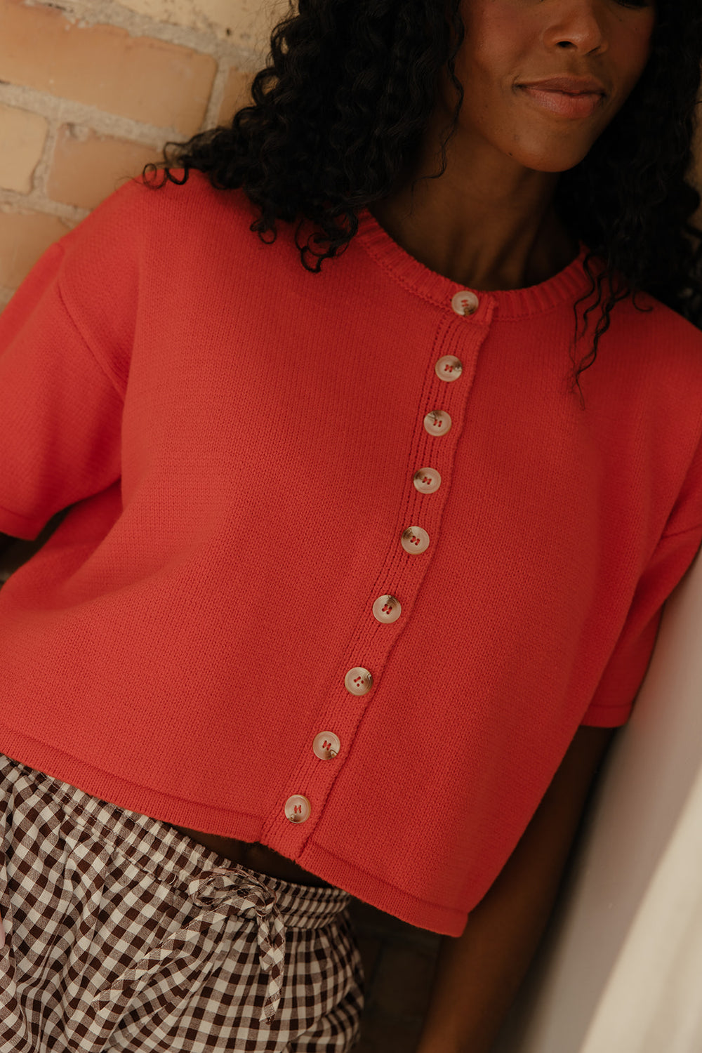 Person wearing a red short-sleeve cardigan with button details, standing against a neutral background.
