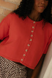 Person wearing a red short-sleeve cardigan with button details, standing against a neutral background.