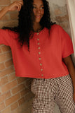 Person wearing a red button-up shirt and checkered pants against a brick wall.
