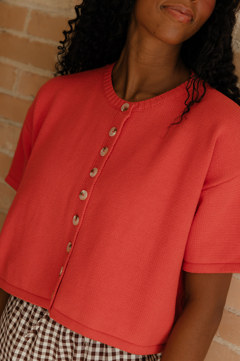 Person wearing a red short-sleeve cardigan with a brick wall background