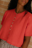 Person wearing a red short-sleeve cardigan with a brick wall background