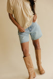 Person wearing a beige shirt, denim shorts, and tan knee-high boots on a beige background