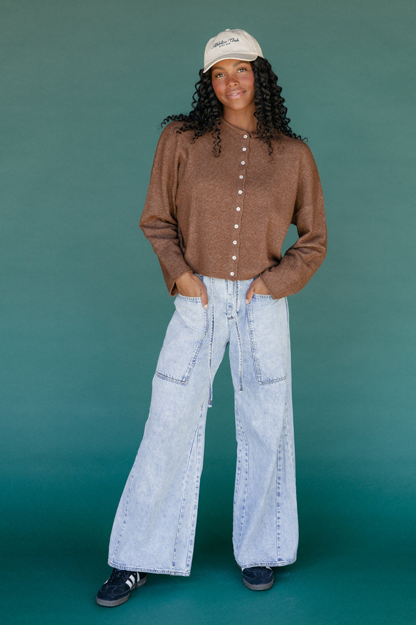 Person wearing a brown shirt and light blue jeans against a teal background