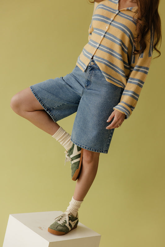 Person wearing a striped shirt, denim skirt, and green shoes on a yellow background