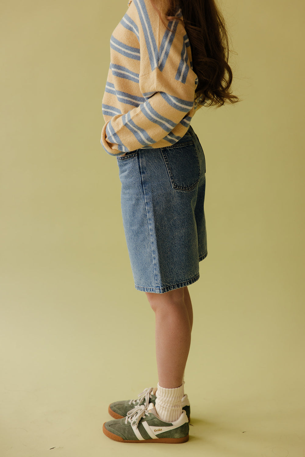Person wearing a striped sweater and denim skirt on a plain background