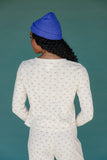 Person wearing a blue beanie and white patterned outfit against a teal background