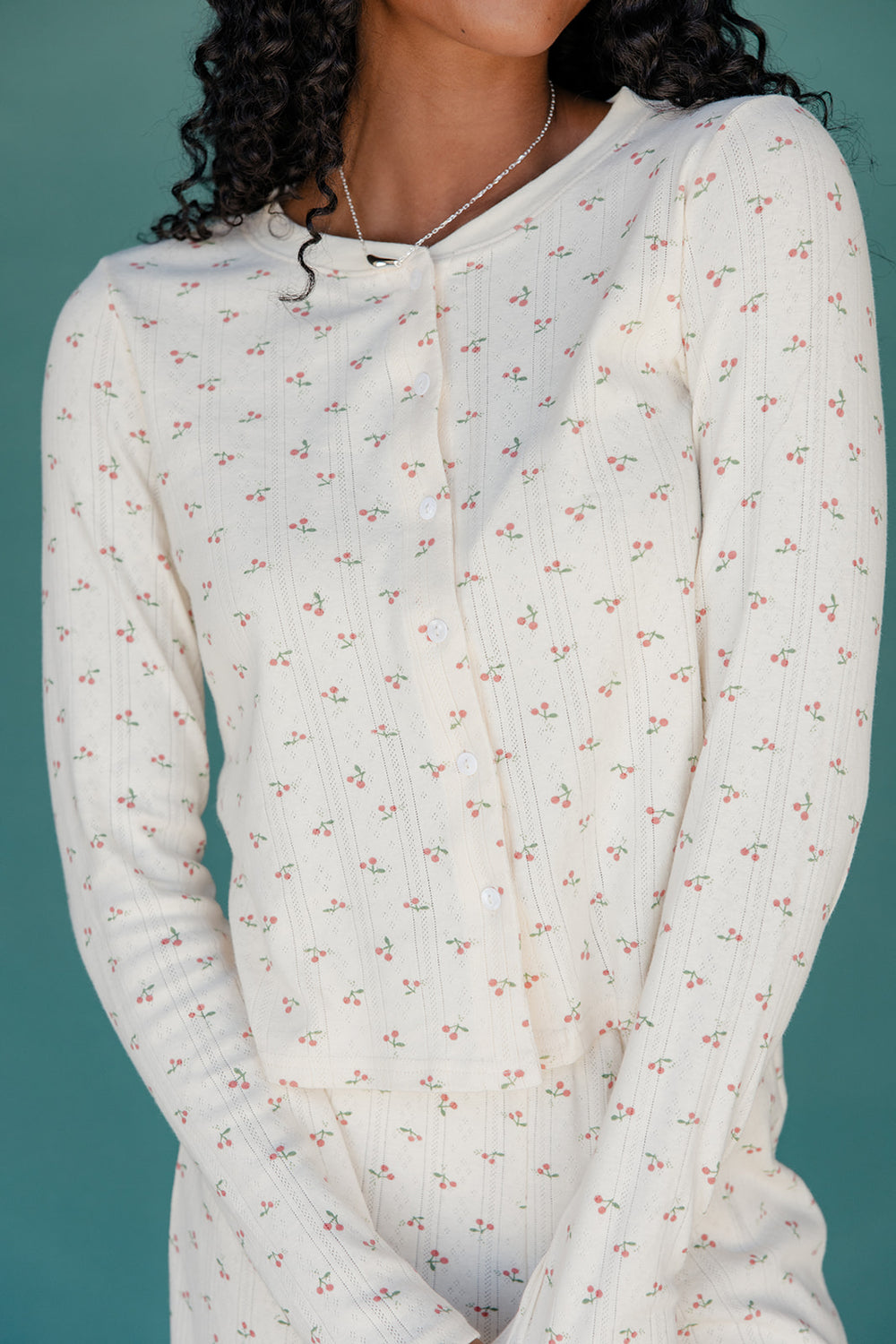 Close-up of a person wearing a white long-sleeve top with a subtle pattern against a teal background