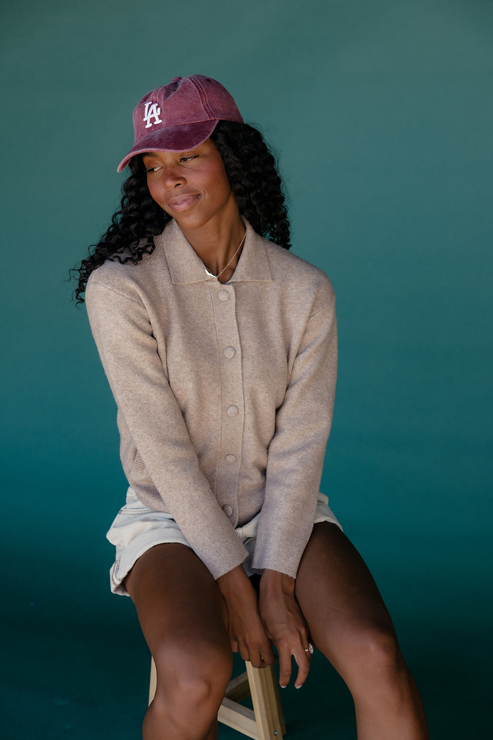 Woman wearing a beige cardigan and purple cap against a teal background