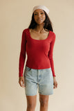 Woman wearing a red long-sleeve top and denim shorts on a beige background