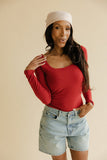 Woman wearing a red long-sleeve top and denim shorts against a beige background