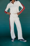 Person wearing a white tracksuit with red and blue stripes on a teal background