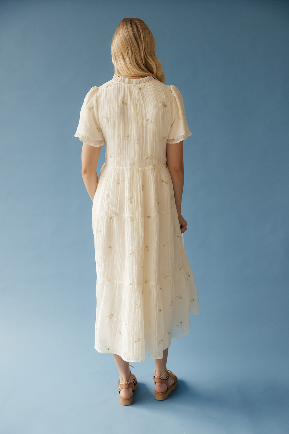 Woman wearing a cream-colored dress with short sleeves against a blue background