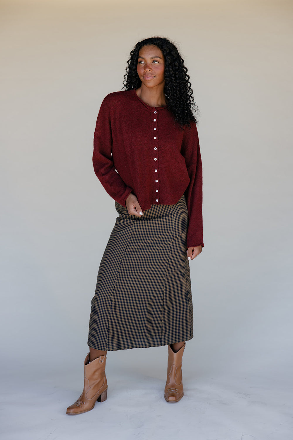 Woman wearing a burgundy button-up shirt and plaid skirt against a plain background