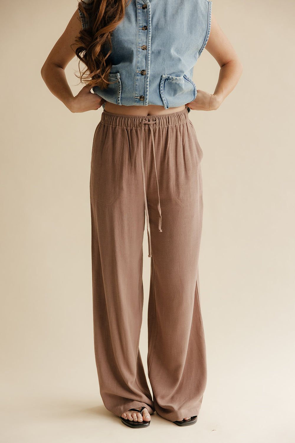 Person wearing a denim vest and brown wide-leg pants on a beige background