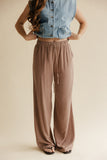 Person wearing a denim vest and brown wide-leg pants on a beige background