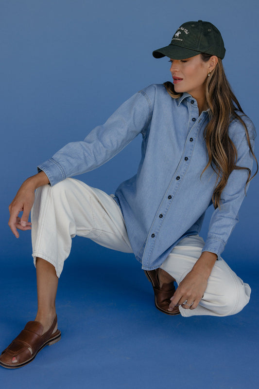 Woman in a blue shirt and white pants posing against a blue background