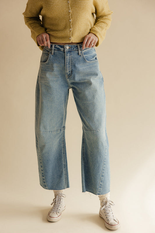 Person wearing a mustard yellow sweater and light blue jeans on a beige background