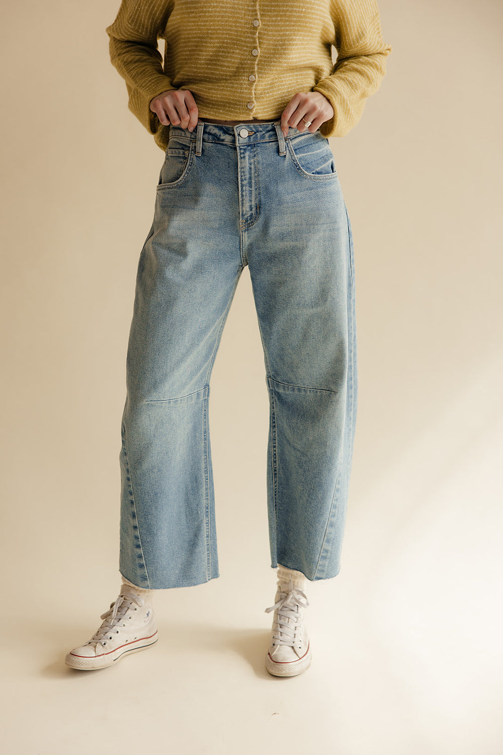 Person wearing light blue jeans and a yellow sweater on a beige background