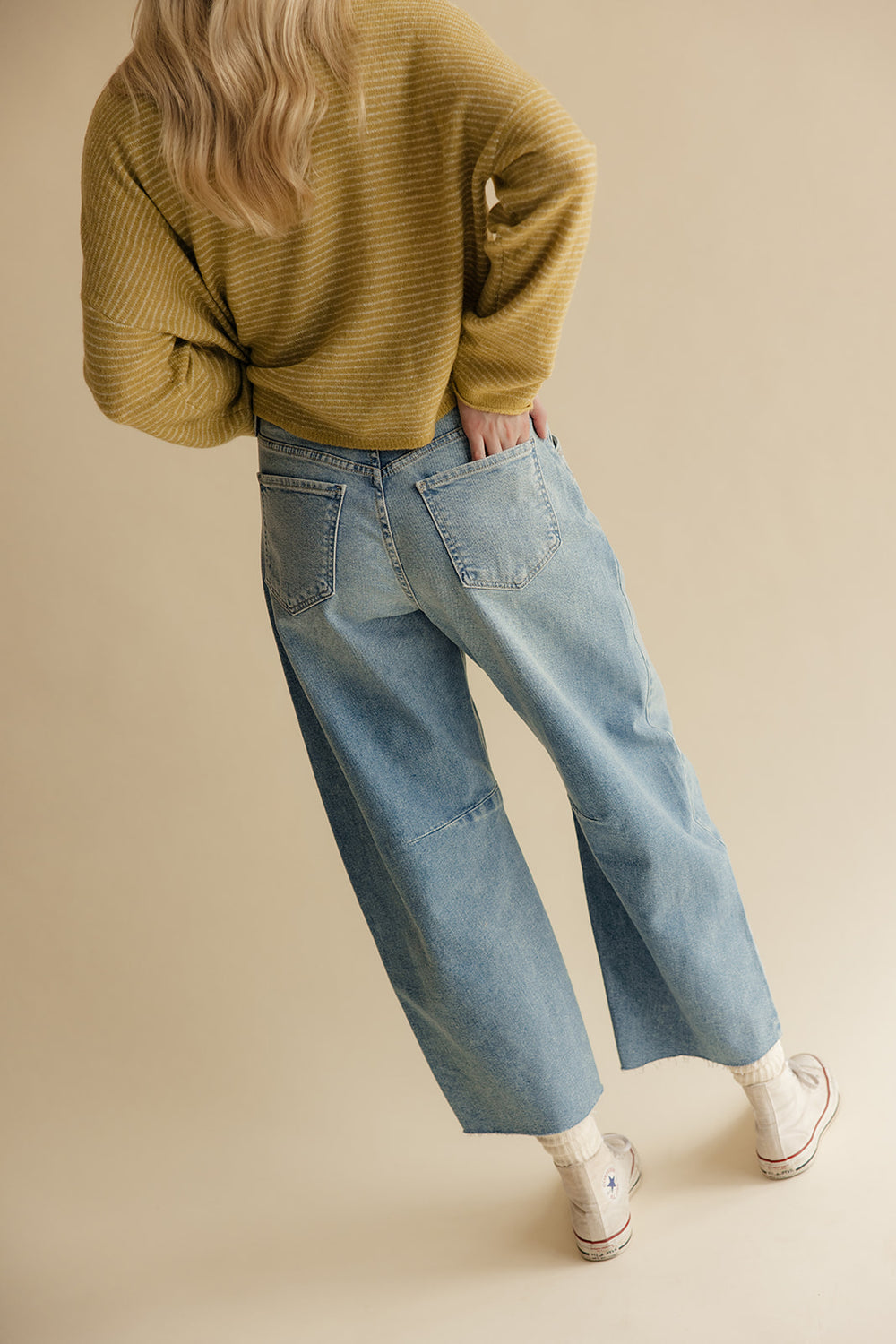 Person wearing a mustard yellow sweater and blue jeans on a beige background