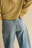 Person wearing a mustard yellow striped sweater and blue jeans on a beige background