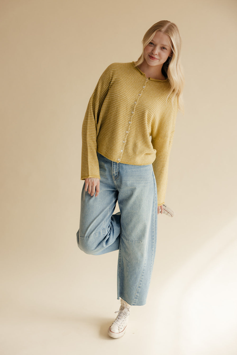 Woman wearing a mustard yellow sweater and blue jeans against a beige background