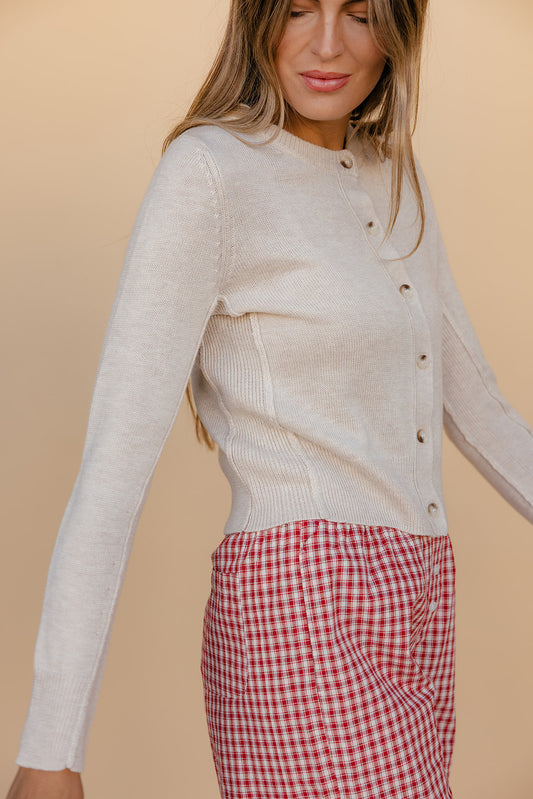 Woman wearing a light gray sweater and red checkered pants against a beige background