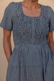 Person wearing a blue and white checkered dress against a beige background