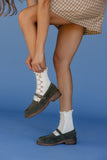 Person wearing green loafers and white socks with lace details on a blue background