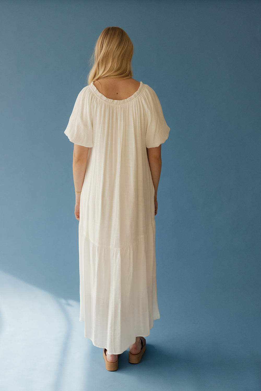 Woman wearing a long white dress against a blue background