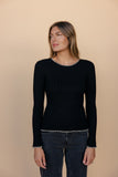 Woman wearing a black sweater with white trim against a beige background