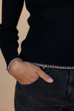 Person wearing a black ribbed sweater with white trim and dark jeans against a beige background